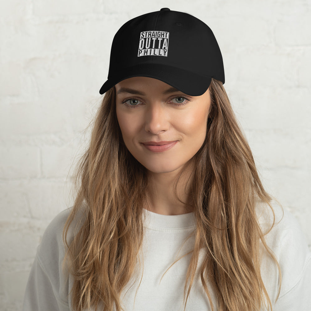 A woman smiling while wearing a black baseball hat with "straight outta philly" embroidered on the front in white.